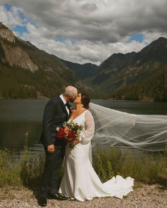 Newlyweds kissing by a mountain lake with a flowing veil.