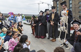 Imge descripton: A group of old fashioned teachers are giving a lesson to a group of chilren and families outside. They hold a skeleton