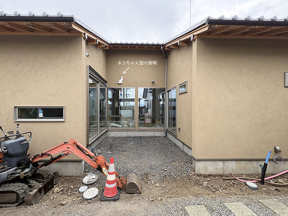 コの字型の建物に囲まれたタイルデッキ施工予定のスペースと、外壁に取り付けたネコ型の照明