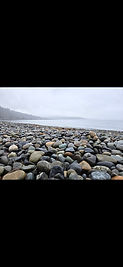 Pebbles on a beach with the sea and sky in the background.