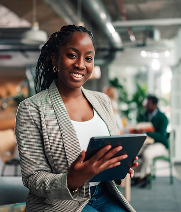 Young black businesswoman smiling at camera, holding a touchscreen tablet inside a modern 