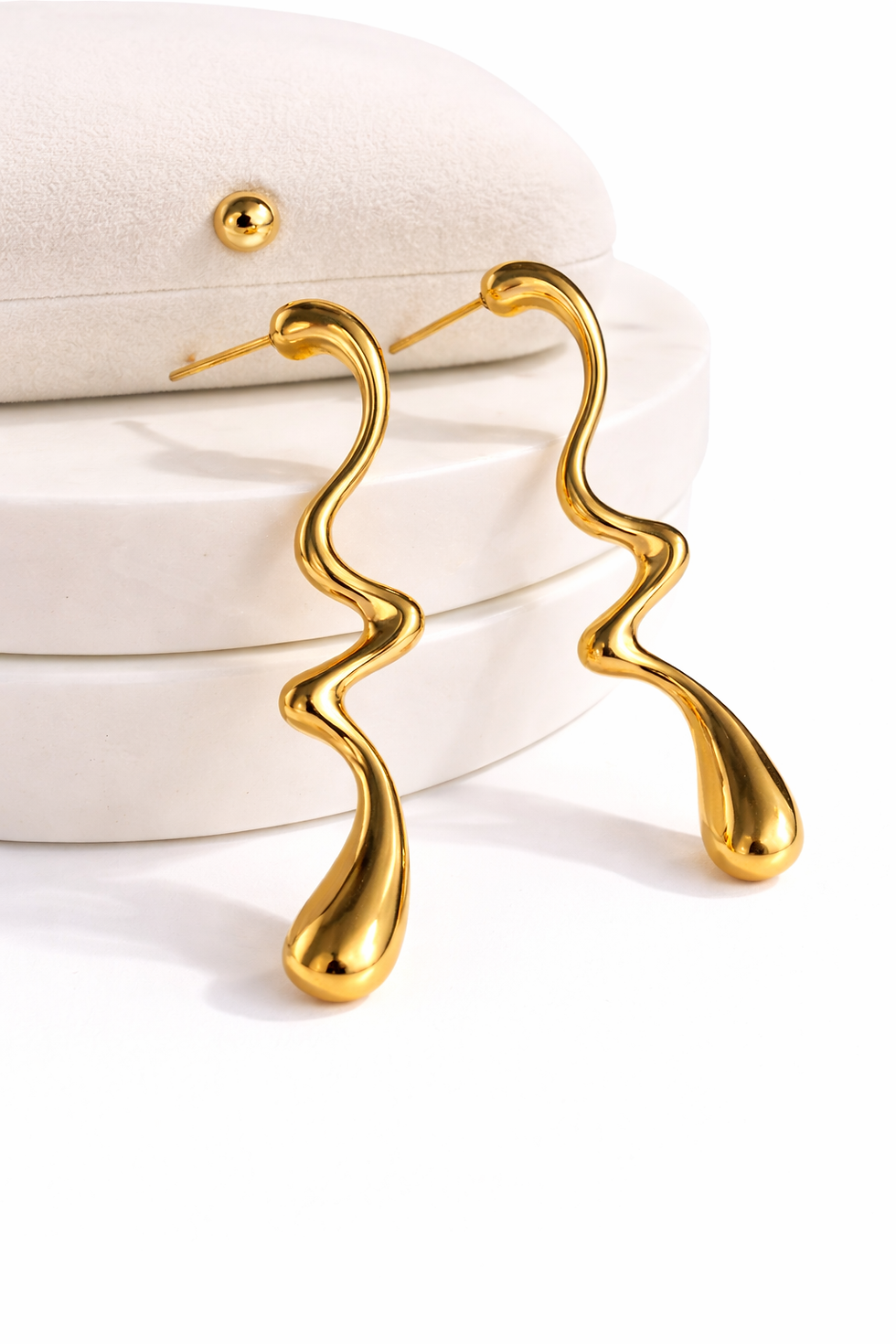 Gold drop earrings with a fluid wavy silhouette and polished finish, displayed on a white jewelry stand.