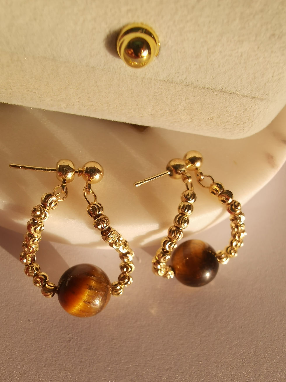 Gold drop earrings with double-chain links and round brown tiger’s eye stone beads, displayed on a cream jewelry stand.