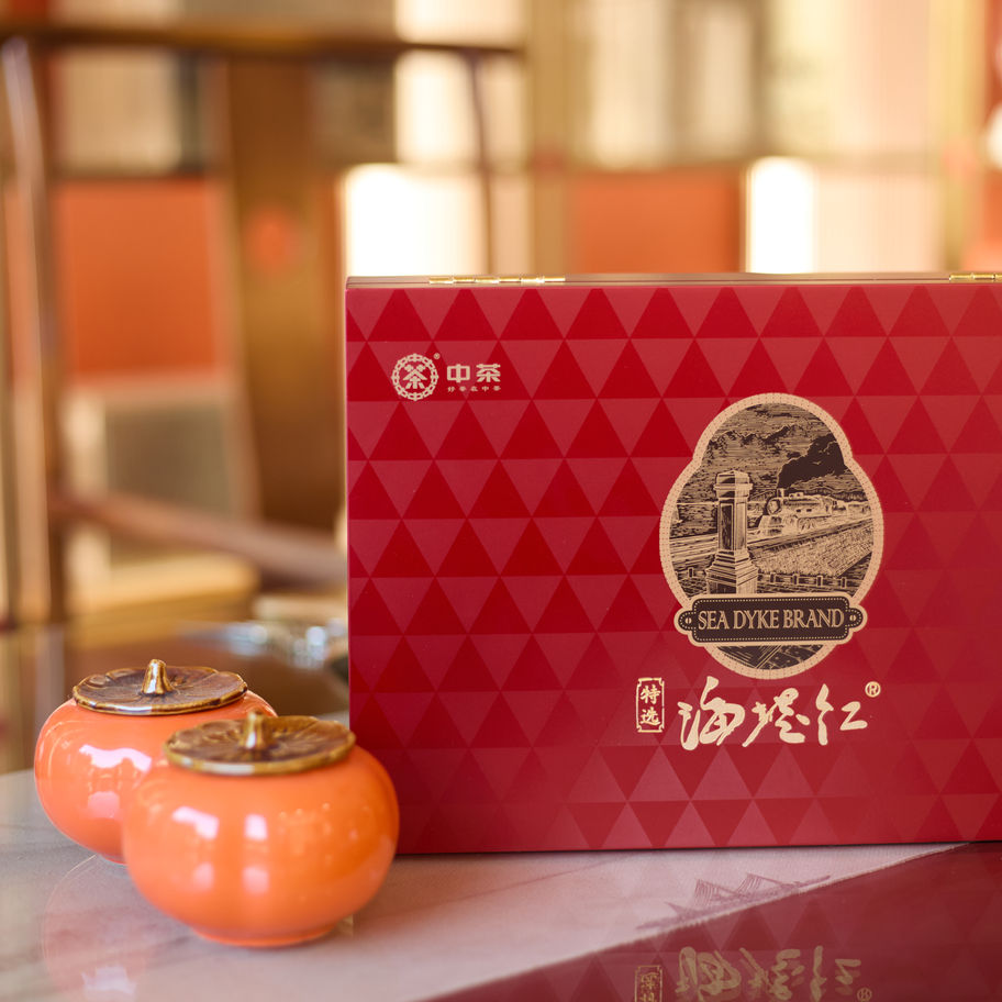 Red Chinese tea gift box with geometric pattern and Sea Dyke brand label, displayed beside two ceramic tea jars on a reflecti