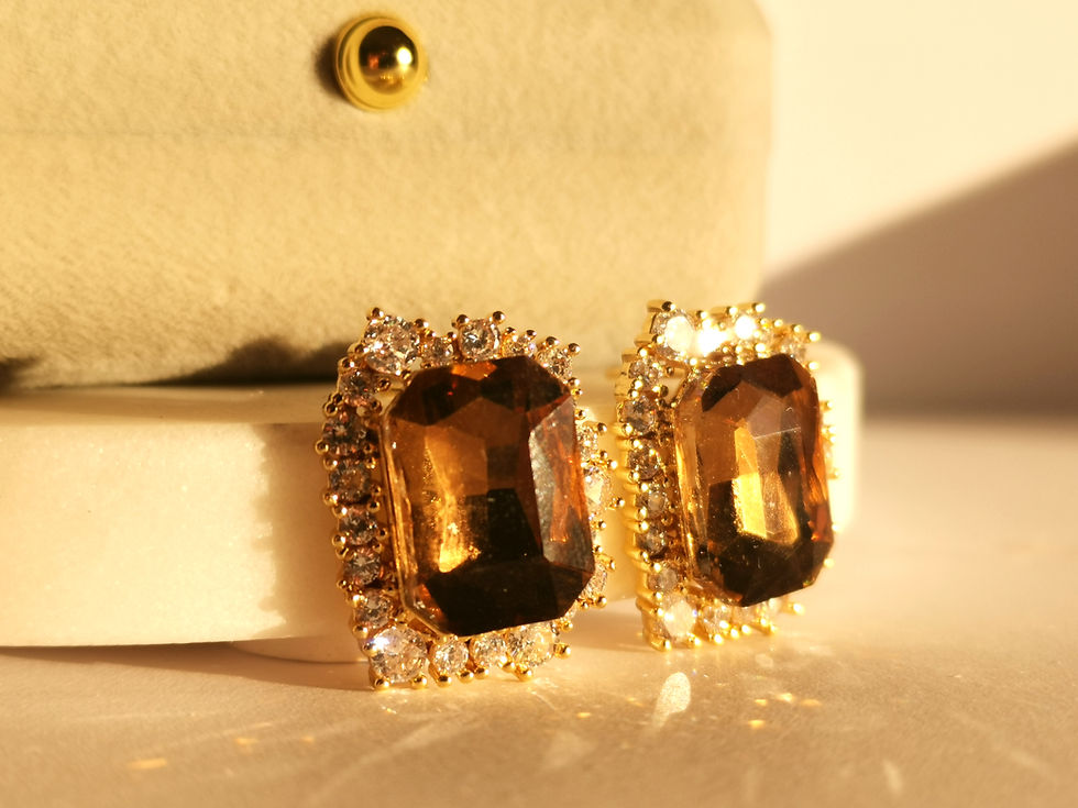 Gold stud earrings featuring rectangular brown gemstones surrounded by a halo of clear stones on a white background.