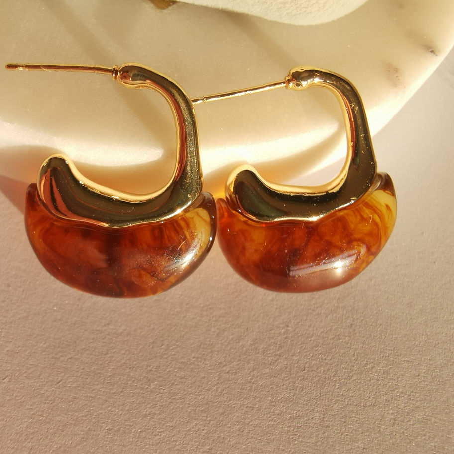 Sculptural gold drop earrings with smooth brown resin accents and a polished modern design on a white background.