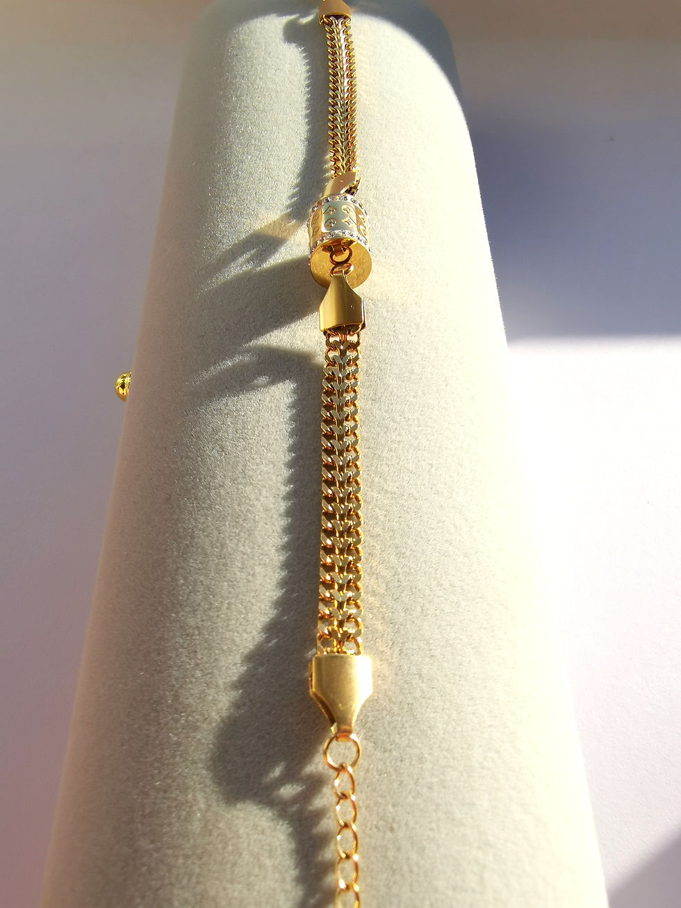 Gold chain bracelet with a chunky woven design, adjustable extender chain, and a cylindrical center charm accented with clear