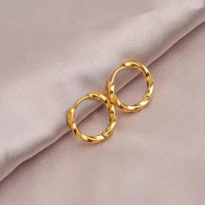 Twisted gold hoop earrings with a polished finish, displayed on a light wooden surface.