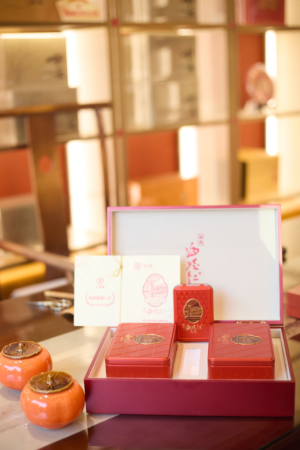 Red Chinese tea gift box with geometric pattern and Sea Dyke brand label, displayed beside two ceramic tea jars on a reflecti