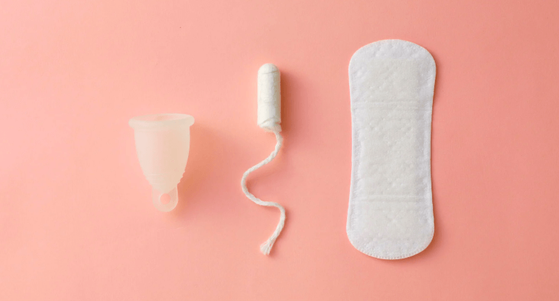 Menstrual cup, tampon, and pad on a pink background, arranged in a row. The scene is clean and minimalistic, highlighting personal hygiene. Period Poverty in Vidarbha