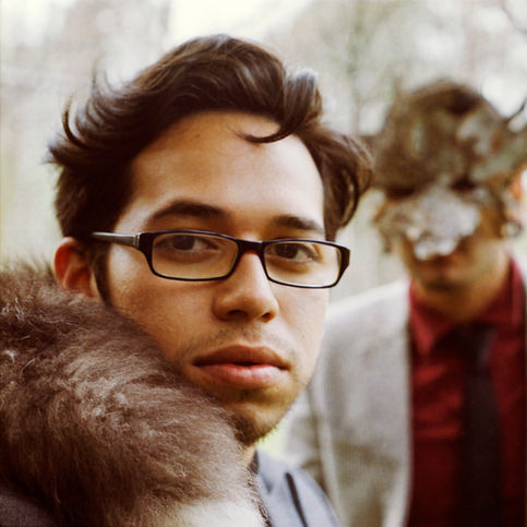 Close-up cinematic portrait of a man with glasses and a fur collar, featuring a masked figure in the background with dramatic, high-contrast lighting. Fine art photography by GLoTography.