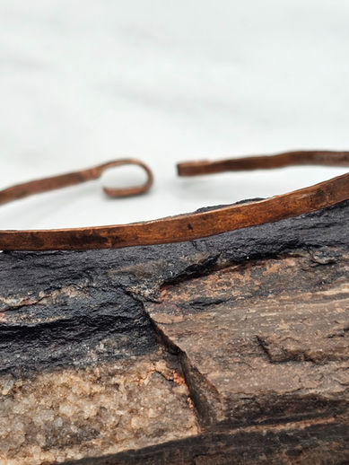 Delicate clasping copper bangle on petrified wood with white marble background