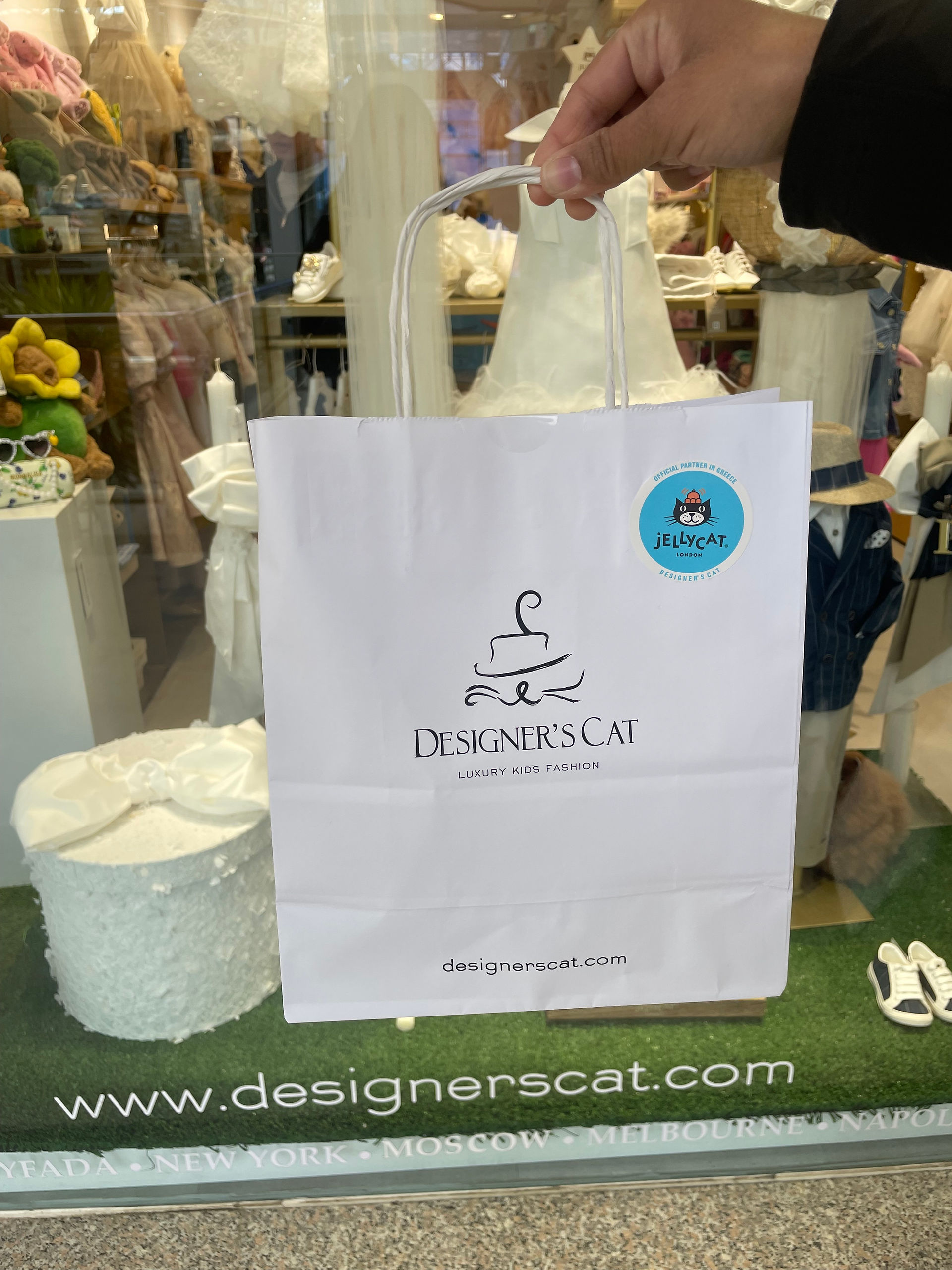 A cute Jellycat plush toy next to a Designer's Cat boutique shopping bag inside the Glyfada mall store.