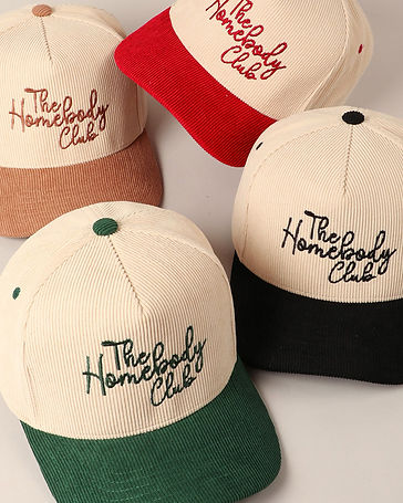four baseball hats in different colors that say the homebody club written in cursive embroidery