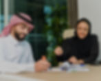 Two Arab business people reviewing documents, smiling and collaborating at desk.
