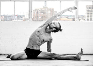 Male yogi in a seated side stretch with the DTLA skyline 