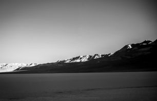 Infrared sunrise over Badwater Basin in Death Valley National Park with distant snow-touched mountains glowing in early light above the dark desert basin, minimalist fine art landscape photography.