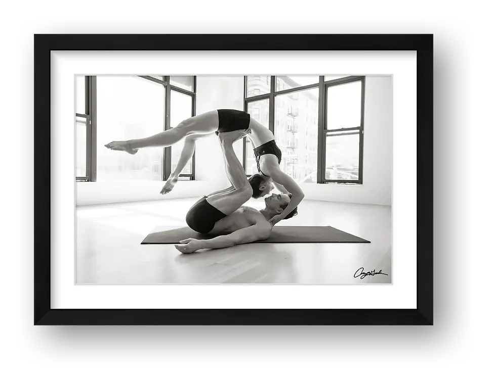 Thumbnail: Black and white acro yoga portrait of two athletes performing a partner balance pose indoors with large windows and city