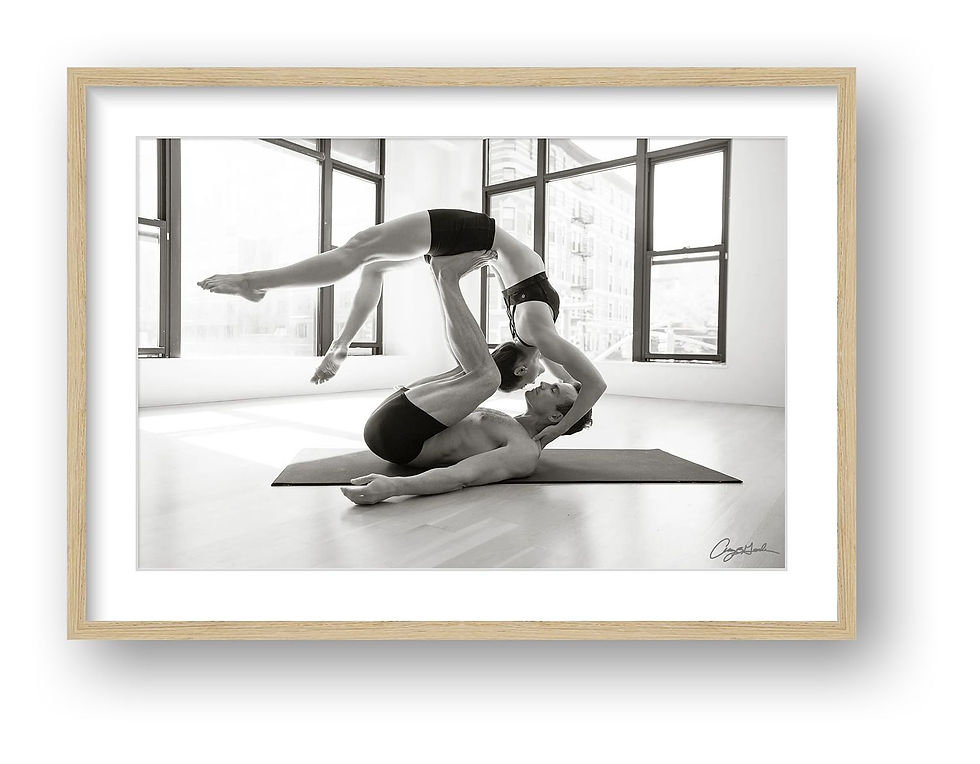 Thumbnail: Black and white acro yoga portrait of two athletes performing a partner balance pose indoors with large windows and city