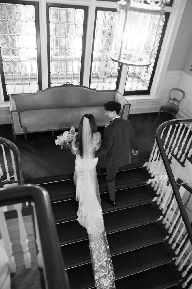 Bride and groom ascend grand staircase, black and white wedding editorial style photo.