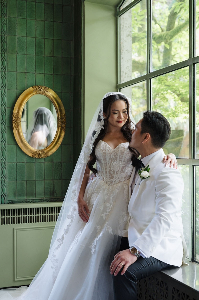 Bride and groom posing by a window with green walls.