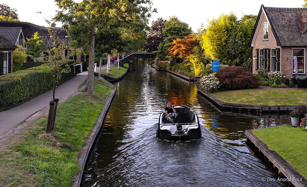 Boat travelling along a canal in Giethoorn with traditional houses and gardens