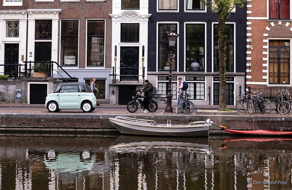 A local cyclist riding a bicycle next to a small microcar parked on a stone canal street at 9 AM as the city wakes up.