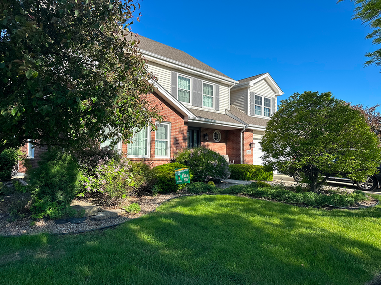 Front yard with small trees and bushes, brick edging, and cut grass.