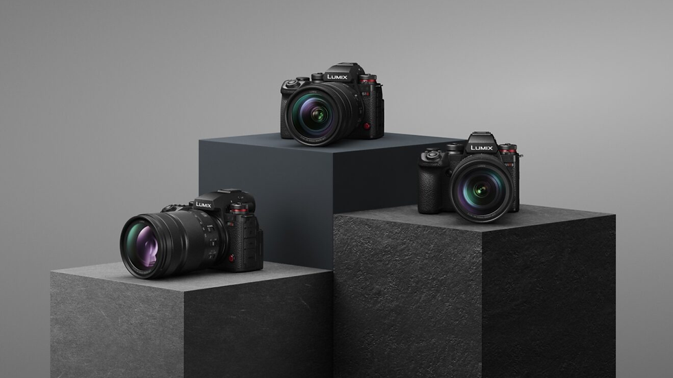 Three Lumix mirrorless cameras on gray and black pedestals against a plain gray backdrop, lenses facing forward.