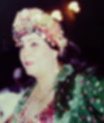 Woman wearing gold jewelry in a large decorated headband with a open ruffled polkadot dress and beaded blouse