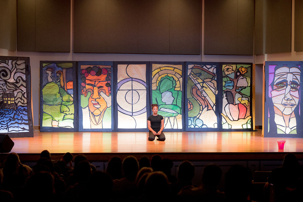 Dancer, dressed in black, kneels center stage during dramatic solo. Stage backdrop is made of visual art that represents bible stories.
