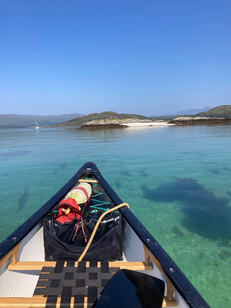 View from an open canoe crossing clear turquoise sea towards rocky islands on the west coast of Scotland.