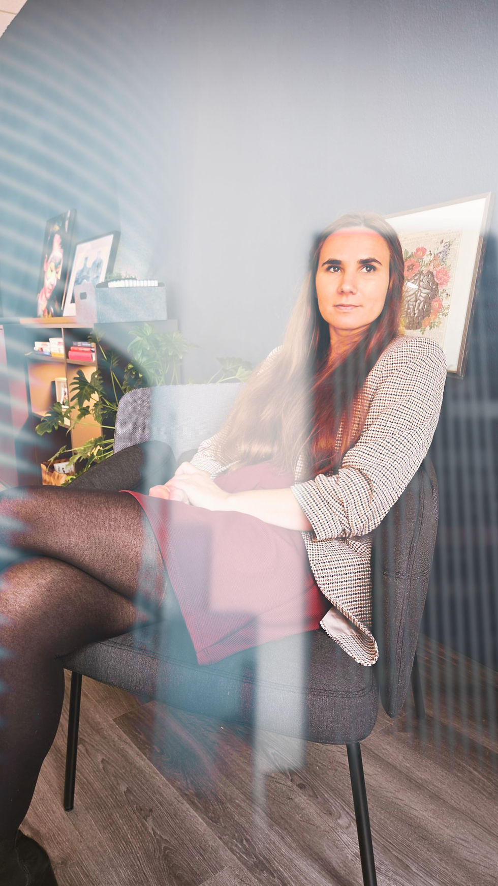 Alison Marburger sitzt nachdenklich in einem Coachingraum auf einem Stuhl, im Hintergrund Pflanzen und Bilder. Das Foto vermittelt Ruhe und Reflexion. Es begleitet einen Text über die Selbstzweifel vieler Eltern („Bin ich gut genug?“), die Suche nach Orientierung und den Druck durch Vergleiche mit der Norm.