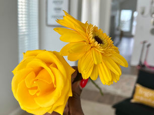 a yellow rose and a yellow sunflower with a yellow pillow with white writing on it is in the background