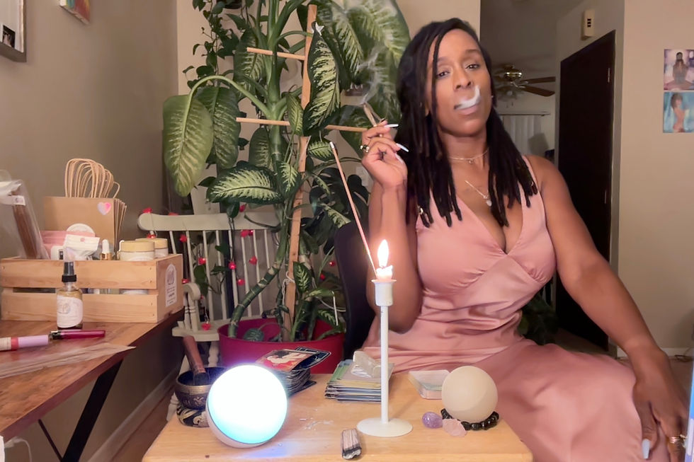Natasha of Naturally U Cosmetics in a pink silk dress smoking a pre roll of her herbal blends. with tarot decks and candles and crystals.