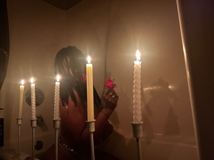 a woman with locs in a bathtub taking a spiritual bath with red flowers and candles lit