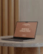 MacBook laptop open on a round stone table in front of a fluted wooden wall.