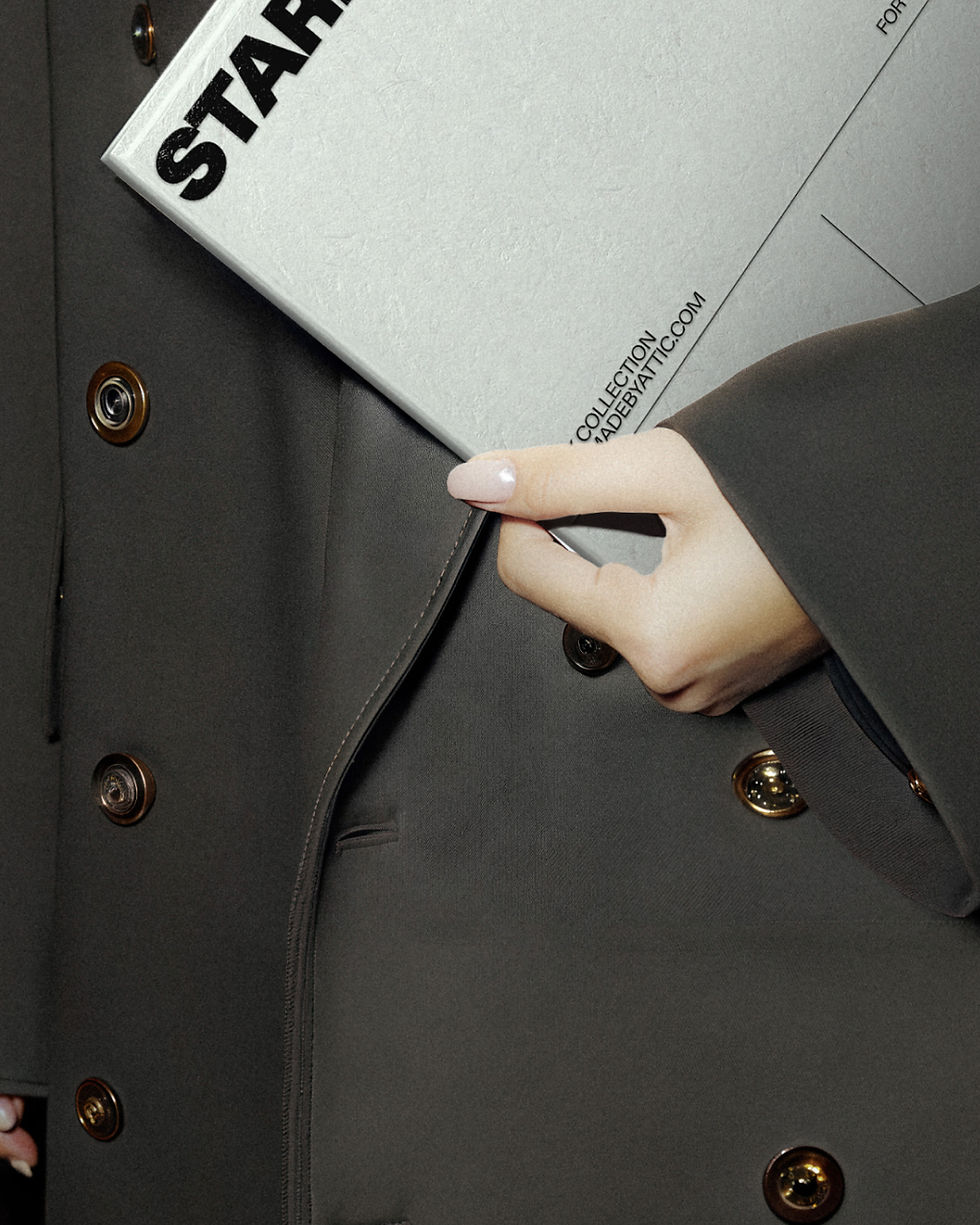 Thumbnail: A high-fidelity brutalist editorial mockup of a grey folder held by a person in a black trench coat against an industrial wir