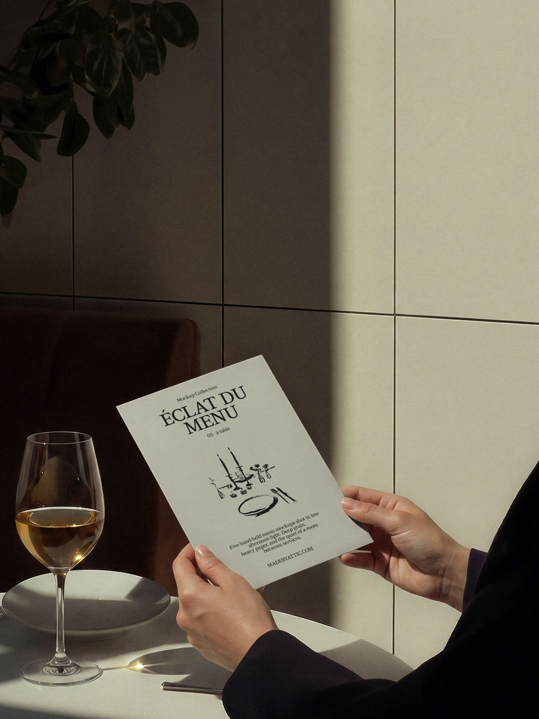 Menu mockup held at an angle at a laid bistro table with a plate and glass of white wine