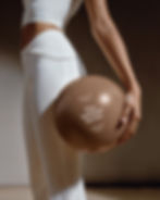 Person in white activewear holding a metallic pilates ball with a branding mockup.