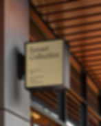 Square white projecting sign attached to a grey column under a modern wood-slatted ceiling.