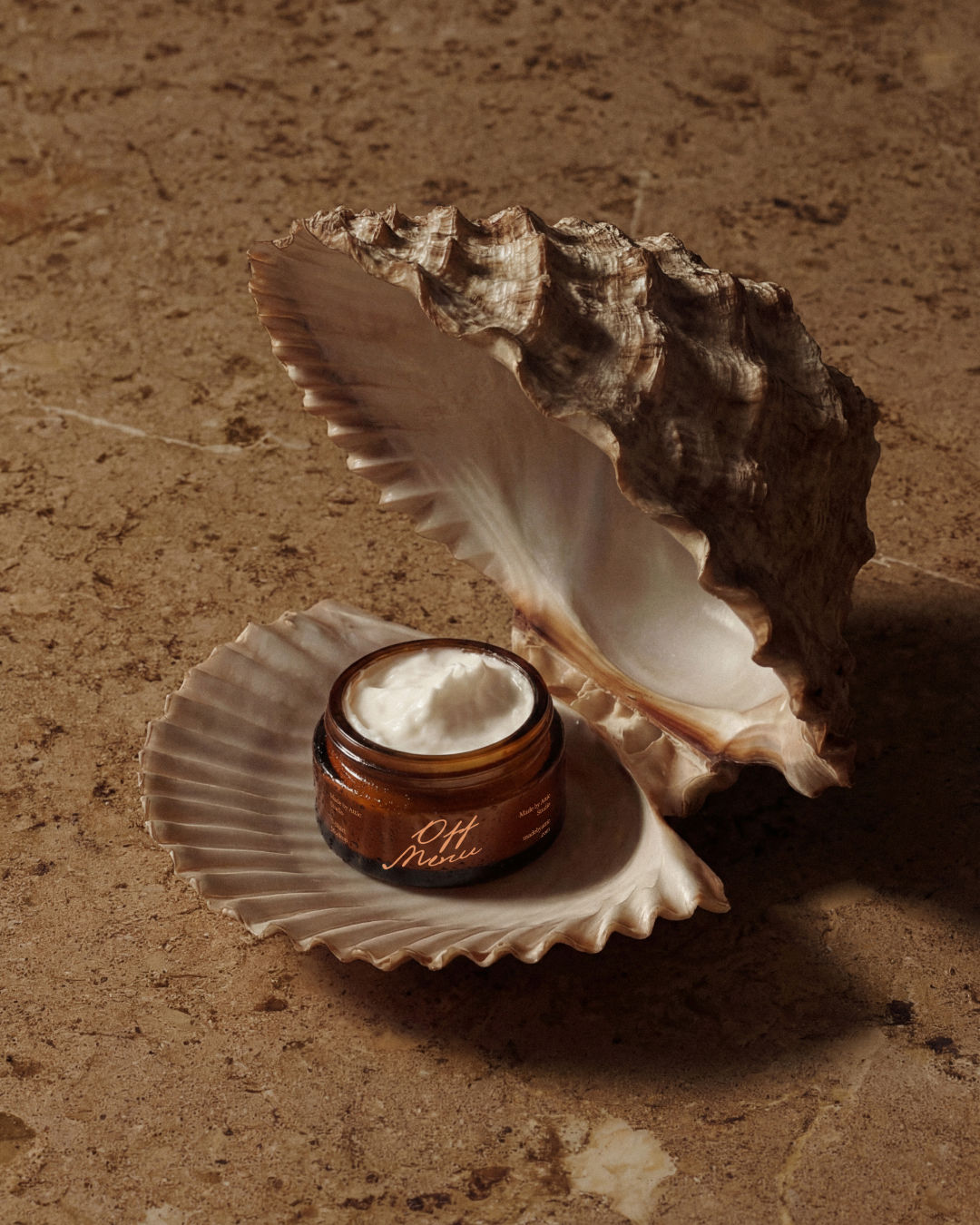 A high fidelity cosmetic jar mockup with an amber glass base and white cream inside, resting inside a large, open seashell on