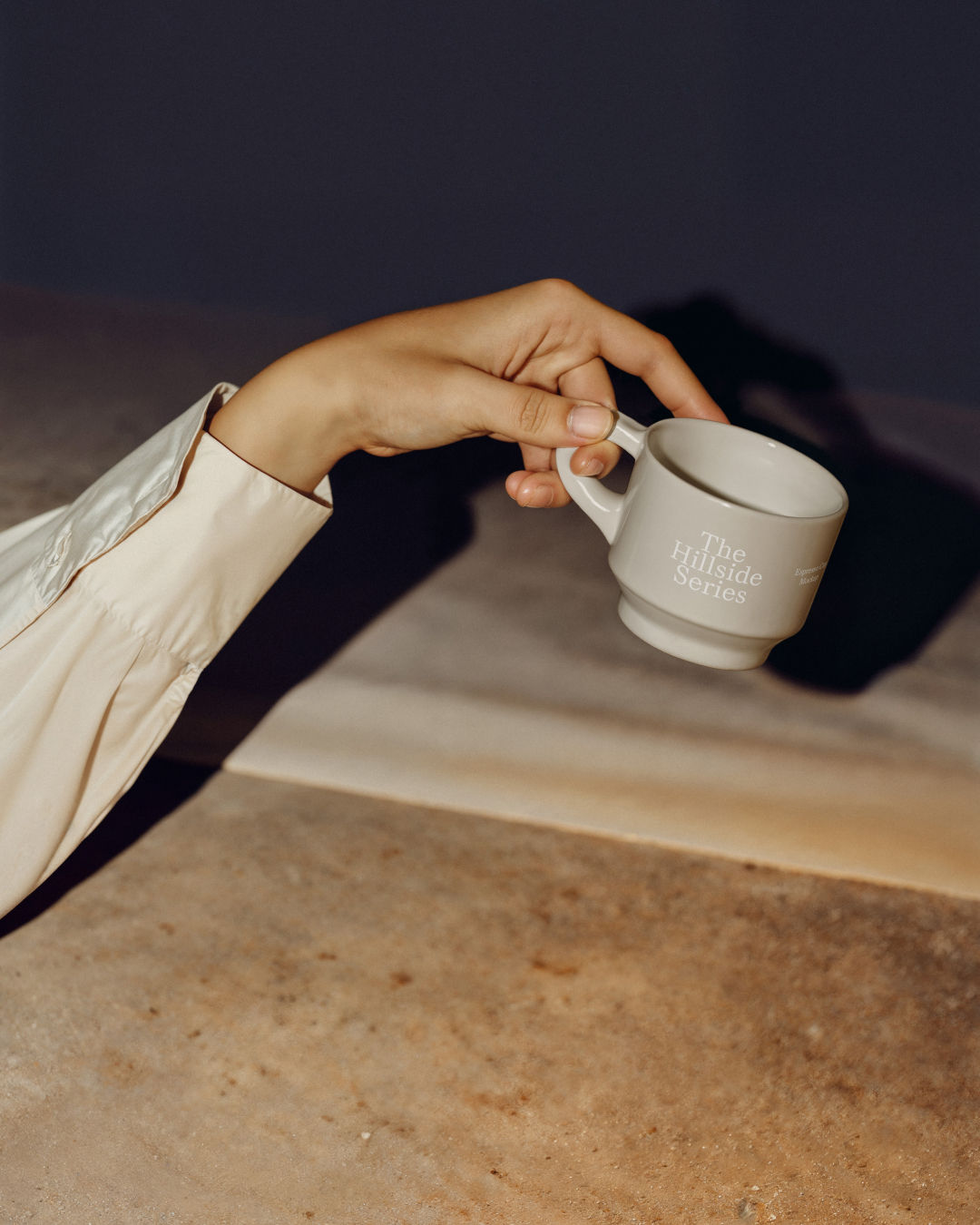 Hand holding a white espresso cup with a sharp shadow cast on a blue and white background.