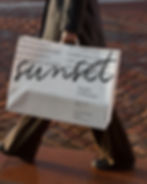 Person walking on city cobblestones holding a large white paper shopping bag in golden hour light.
