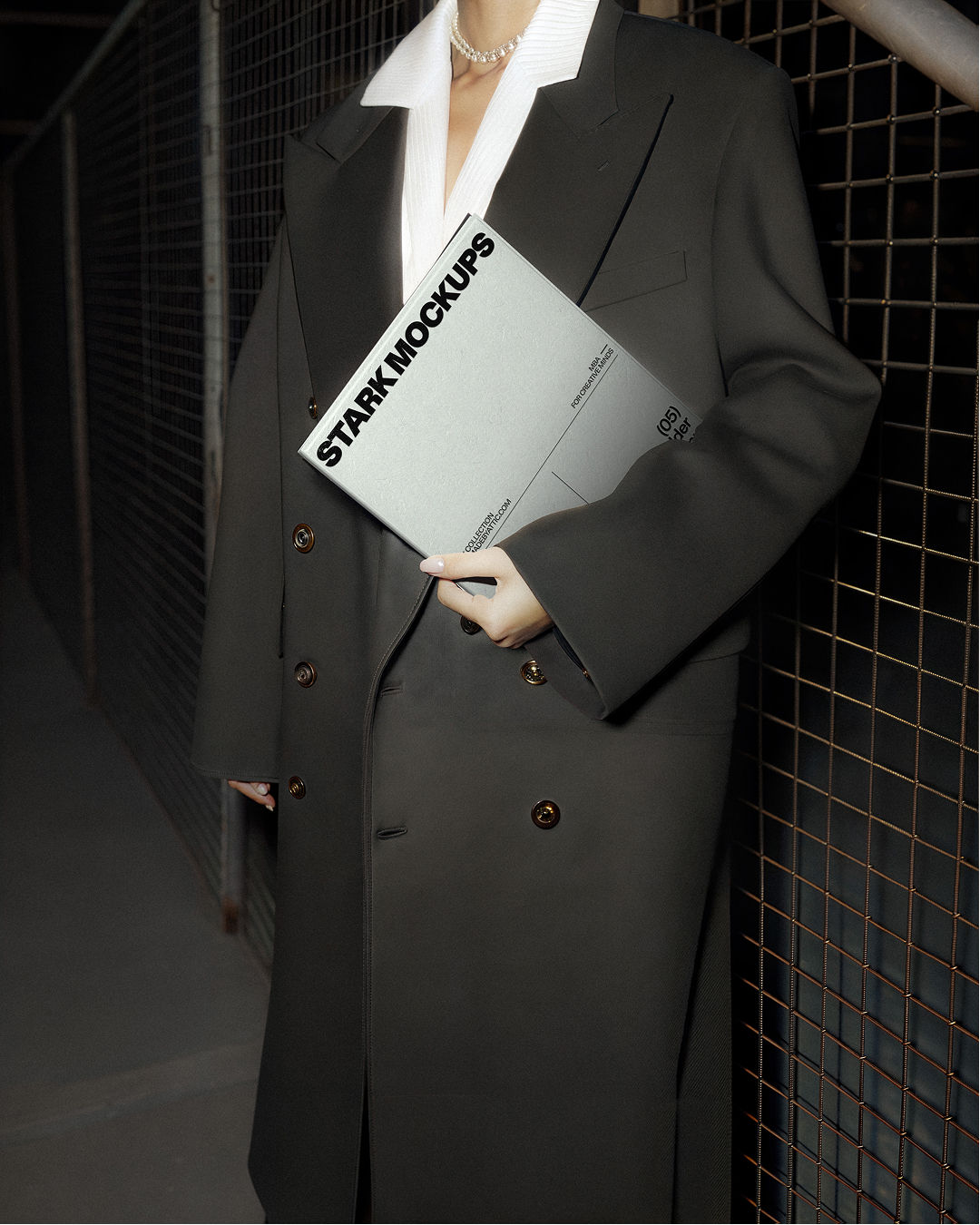 A high-fidelity brutalist editorial mockup of a grey folder held by a person in a black trench coat against an industrial wir