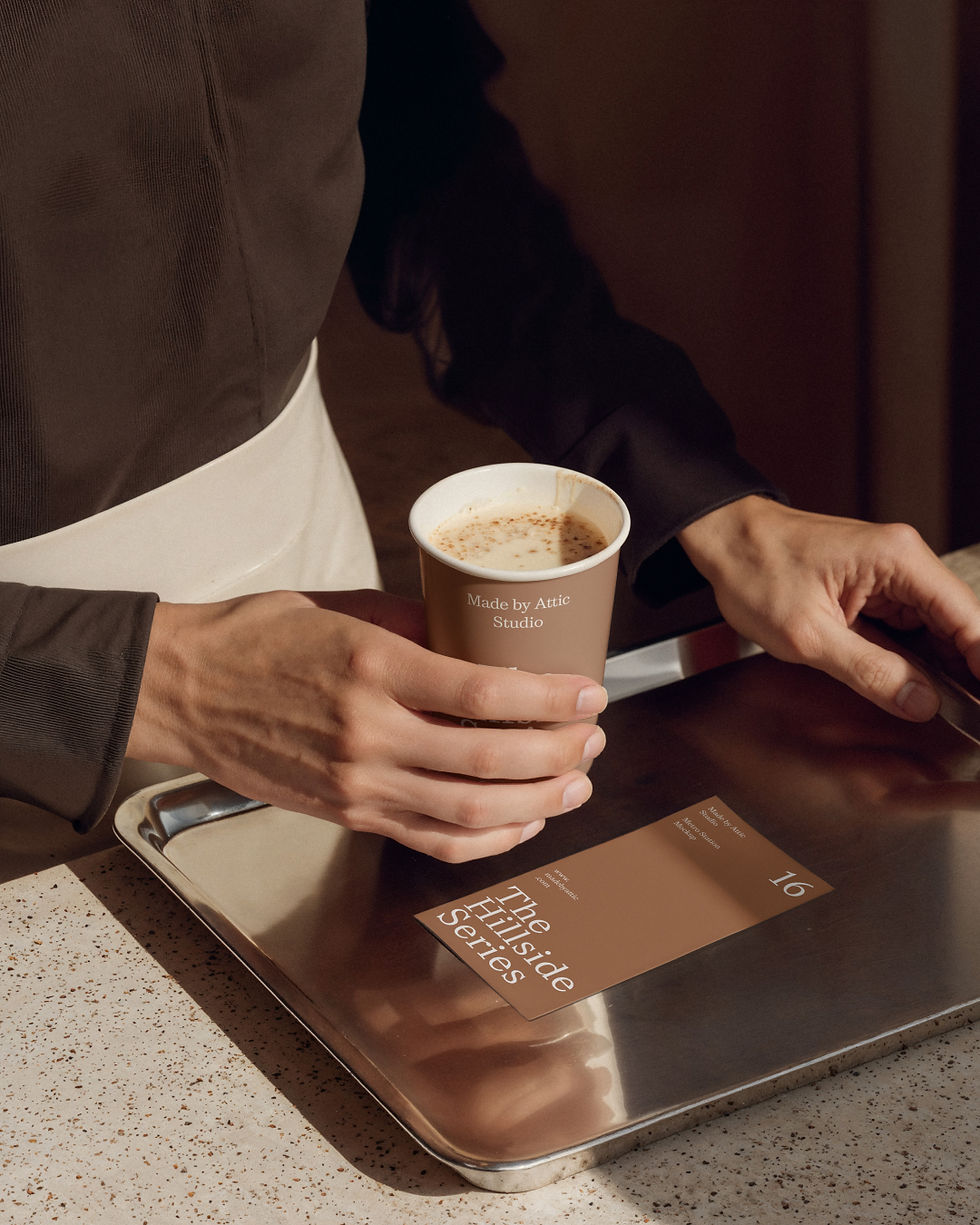 A photorealistic hospitality mockup featuring a barista serving coffee on a silver tray with a branding card.