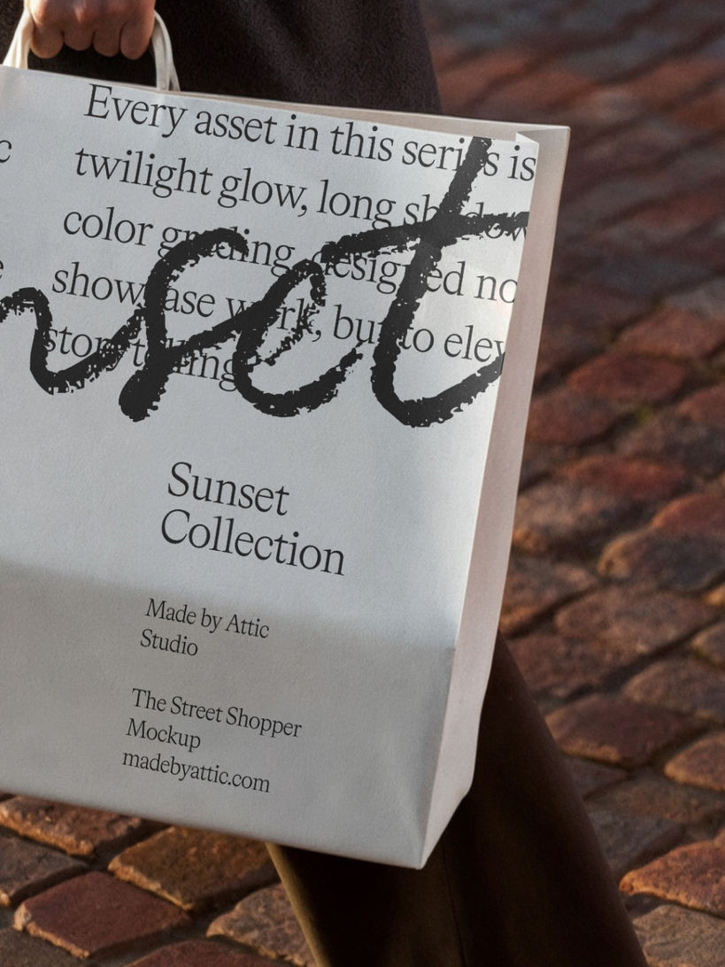 Person walking on city cobblestones holding a large white paper shopping bag in golden hour light.