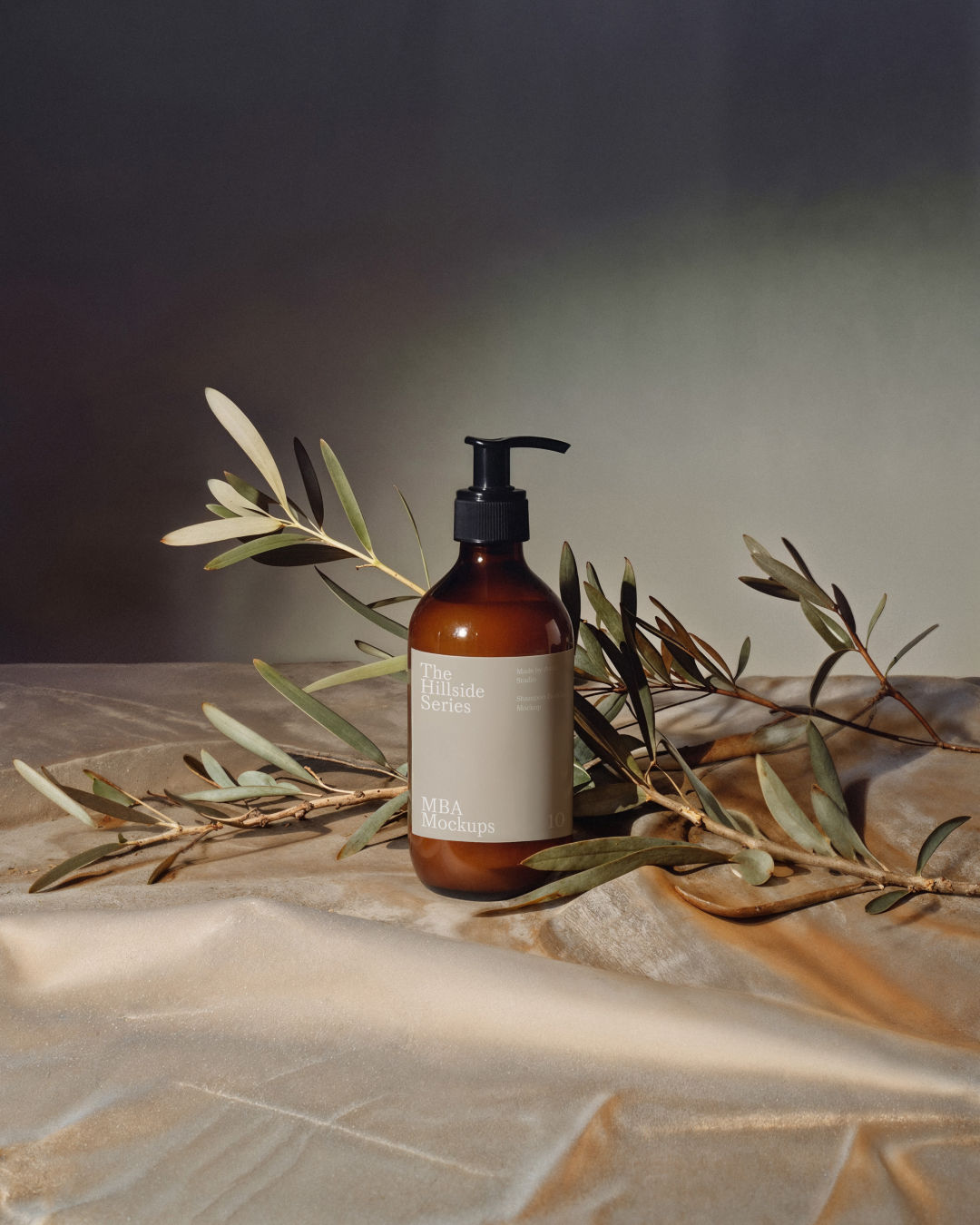 Amber pump bottle standing on stone surrounded by olive branches with leaf shadows on the label.
