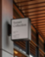 Square white projecting sign attached to a grey column under a modern wood-slatted ceiling.