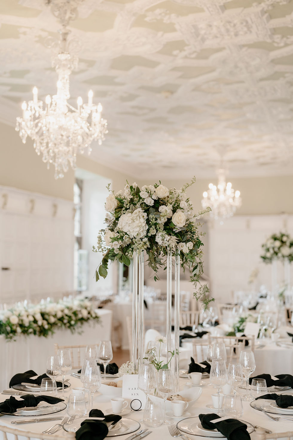 A minimalistic but stylish monochrome wedding breakfast set up on round tables with black napkins paired with crisp white linen and gorgeous floral centrepieces in glass vases